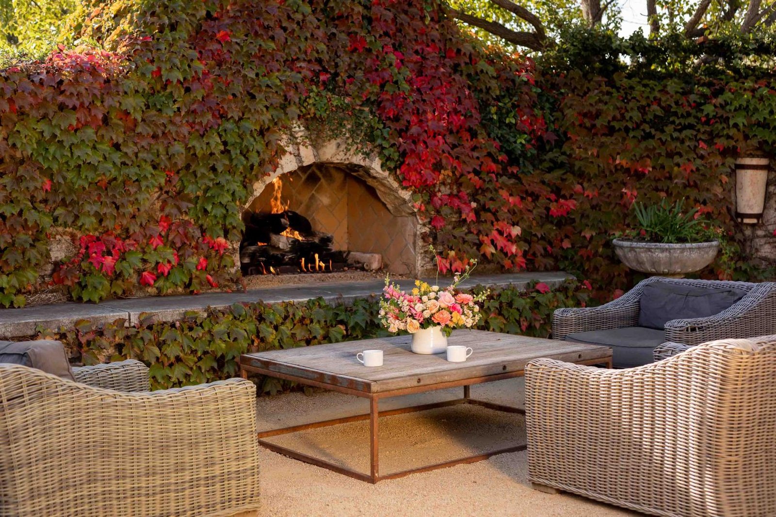 Outdoor Fireplace And Lawn Furniture With Flowers And Two Coffee Cups On The Table